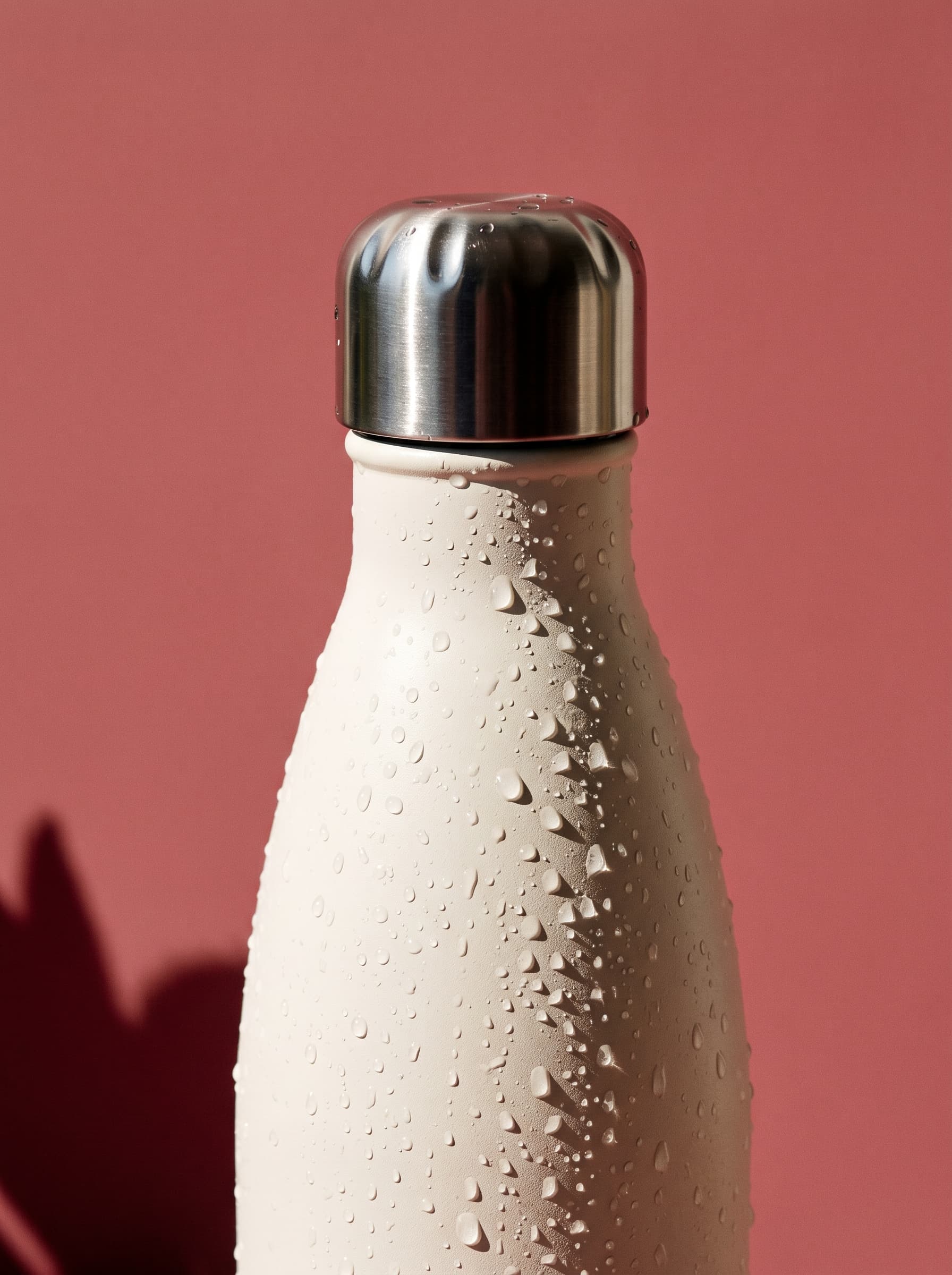 AI product photo: a cream water bottle covered in condensation drops against a dusty red wall